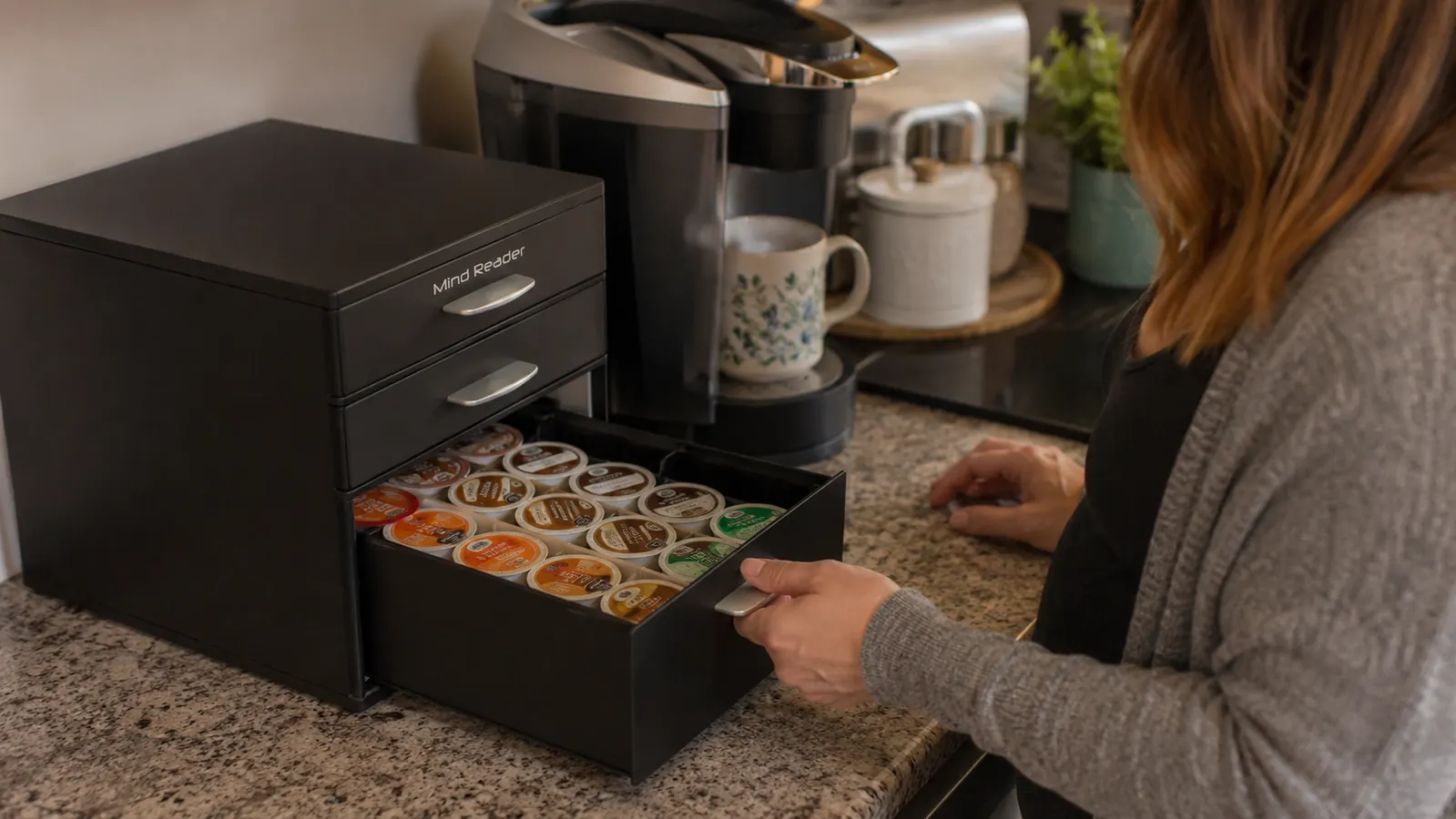 Hand pulling open a drawer of a black K-cup organizer revealing rows of coffee pods sorted by flavor