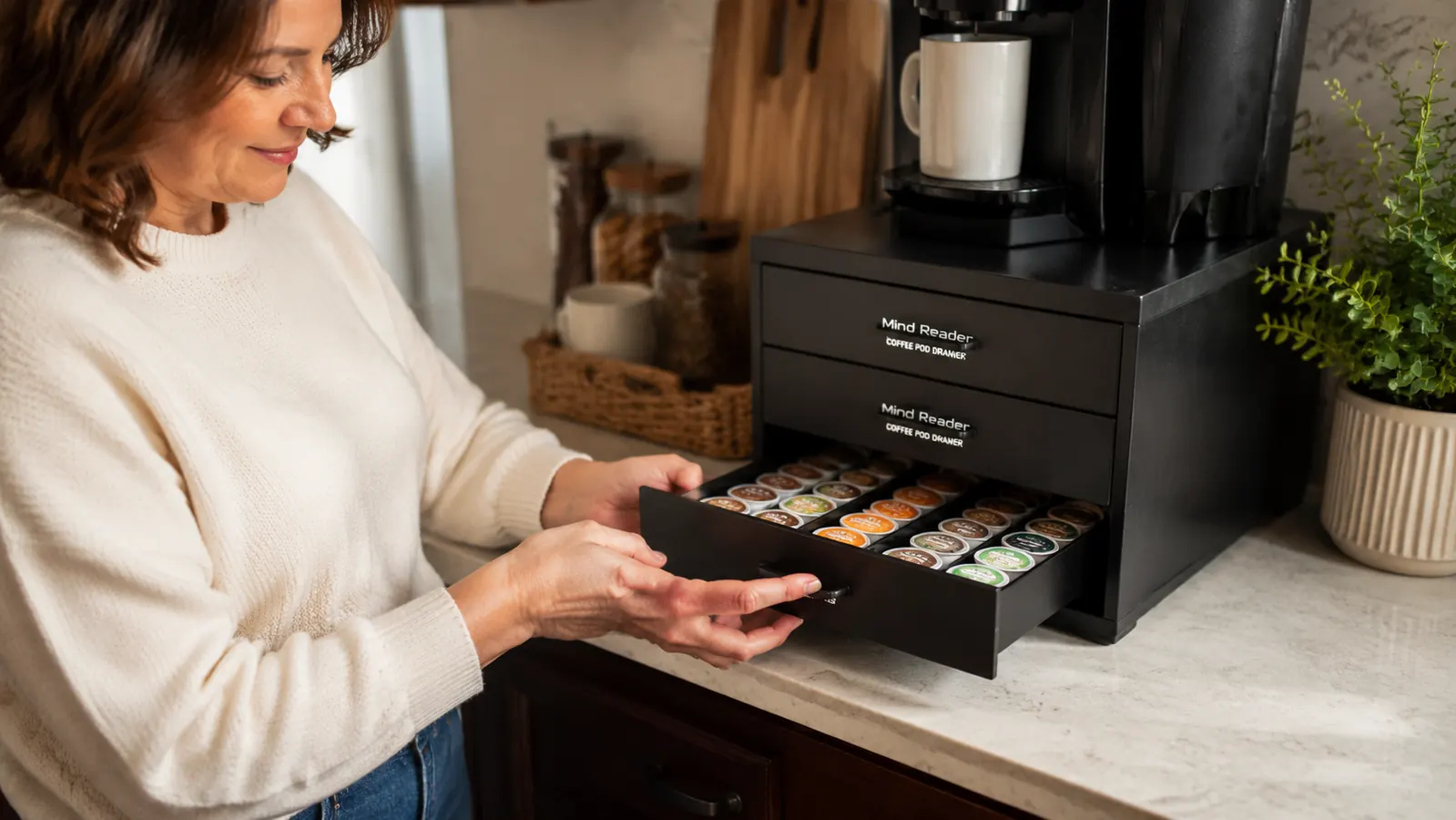 Close-up of a hand sliding open a black three-drawer coffee pod organizer on a countertop, pods sorted by row